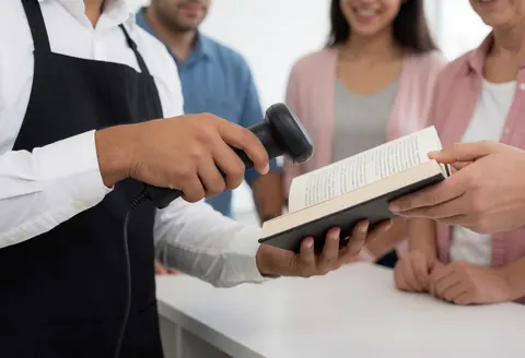 A bookstore employee uses a scanner to process a book held by a customer during a service interaction.