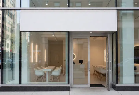 Modern nail salon exterior featuring glass entrance doors and white tables visible from the street