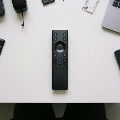 Black universal remote control placed on a clean white table surrounded by electronic components and a laptop for television repair.