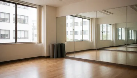 Empty dance studio featuring wooden floors, wall mirrors, and rolled mats in the corner, suitable for dance classes.