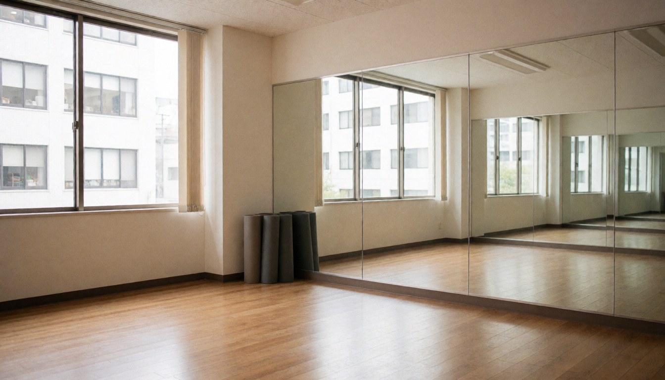 Empty dance studio featuring wooden floors, wall mirrors, and rolled mats in the corner, suitable for dance classes.