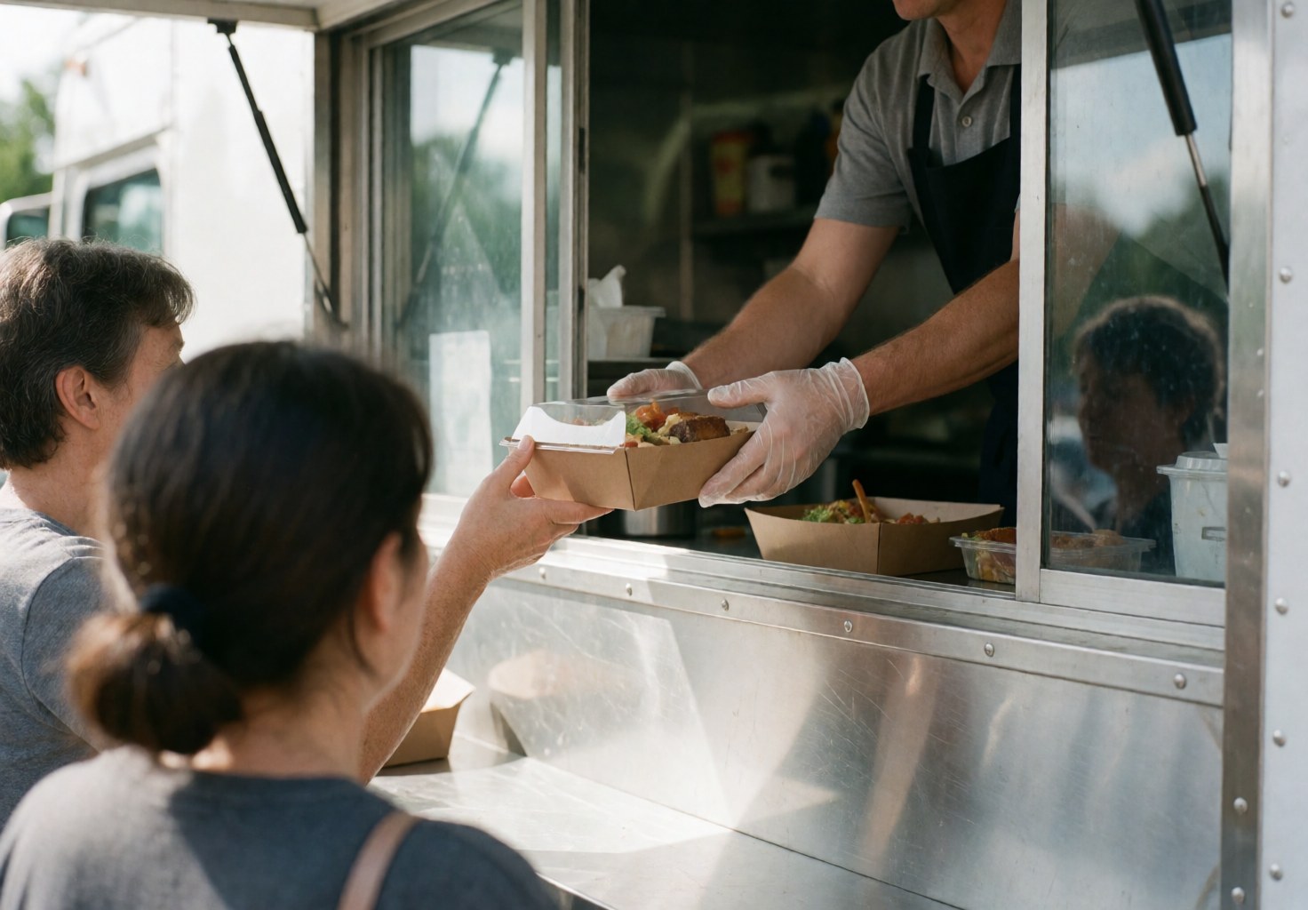 A gloved hand hands a food box to a customer from a food truck, showing fast and clean service.
