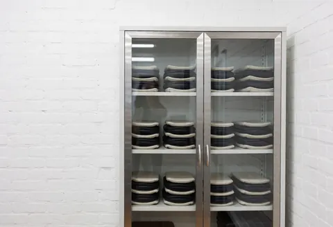 Metal cabinet holding thermal therapy items in a physiotherapy studio with white brick walls and bright clinical lighting