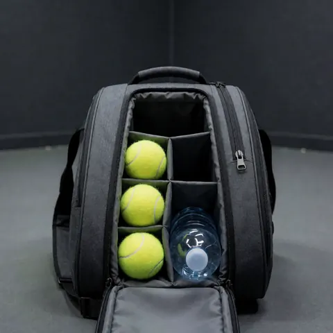 Open tennis bag containing three yellow balls and a water bottle on a gray court surface, ideal for tennis instructors.