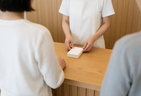 A professional in a white apron organizes appointment cards on a wooden table at a customer service reception area with plank walls.