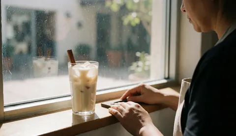 A refreshing glass of horchata topped with cinnamon sitting on a windowsill bathed in natural sunlight, creating a warm and inviting atmosphere for a bed and breakfast.
