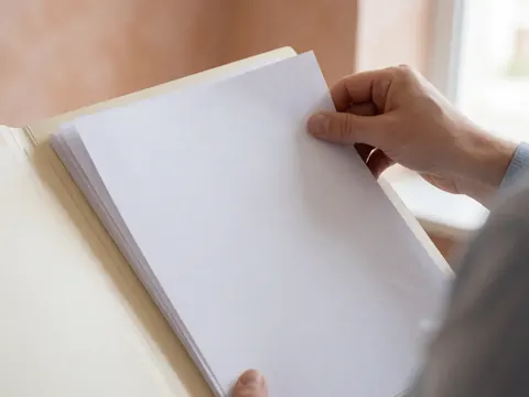 Close-up of a hand organizing white documents inside a folder against a terracotta wall with natural light.