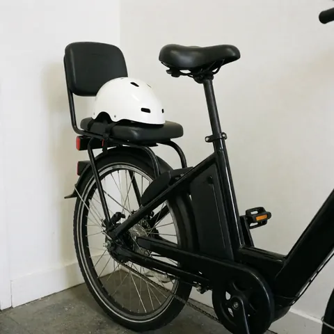 Black electric taxi bicycle with passenger seat and white helmet leaning against a white wall ready for service
