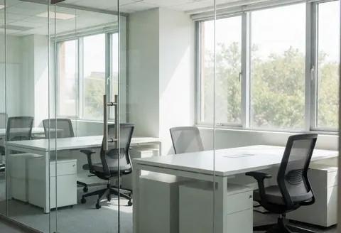 Empty corporate office featuring white desks, black ergonomic chairs, and large windows letting in natural daylight.