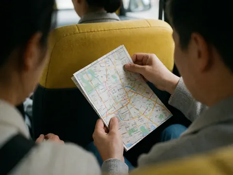 Close-up of hands holding a city map inside a taxi with a visible yellow seat, depicting navigation for transportation services.