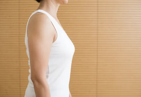 A woman in profile view wearing a white t-shirt standing against a wooden wall background with natural lighting.