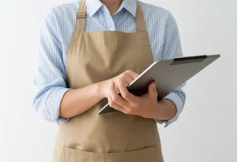 Person wearing an apron and striped shirt using a digital tablet against a white background, suitable for professional services.