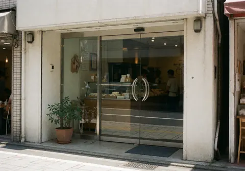 Store entrance featuring a glass door, white walls, and a potted plant with reflections on the glass surface