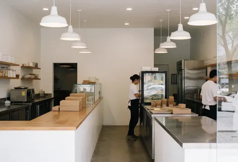 Employees serving cakes in a modern bakery with stainless steel counters and white hanging lights