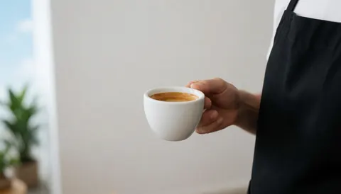 Barista serving espresso in a white cup, white wall and natural light, ideal for coffee shop