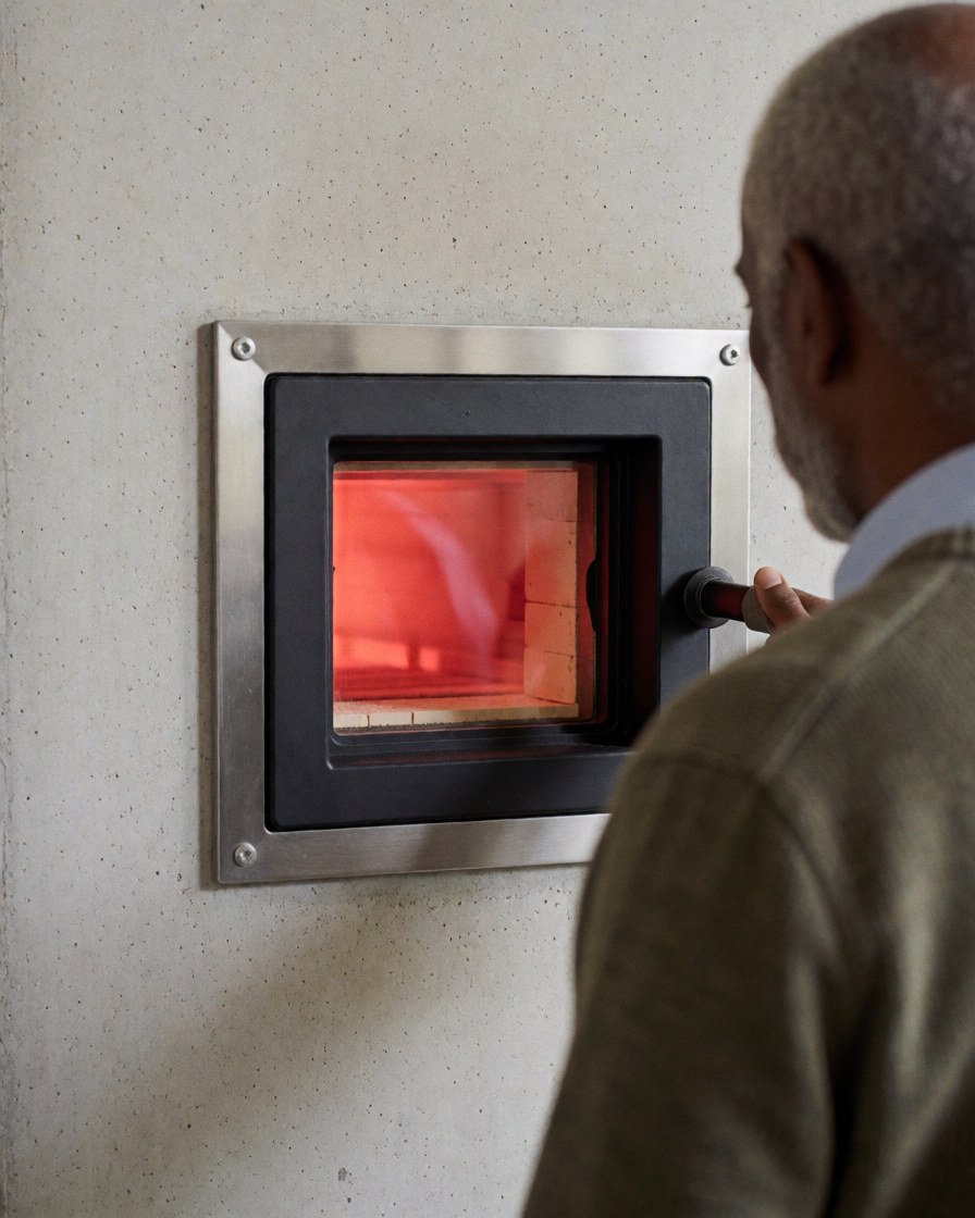 Back view of a customer observing a glowing red pottery kiln inside a workshop with concrete walls
