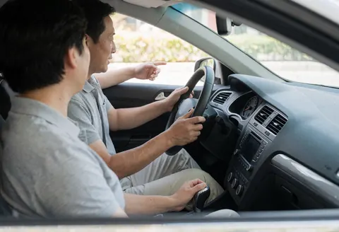 Driving instructor pointing while student operates manual transmission in realistic driving school scene