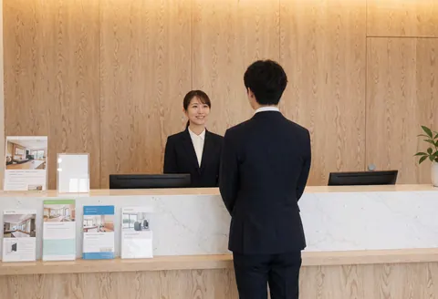 Smiling receptionist showing brochures to a client at a light wood counter with a computer.