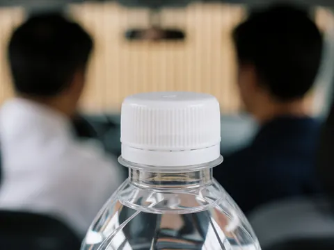 Close-up of a textured water bottle cap with a blurred background featuring light wood walls and two people, suitable for hygiene services.