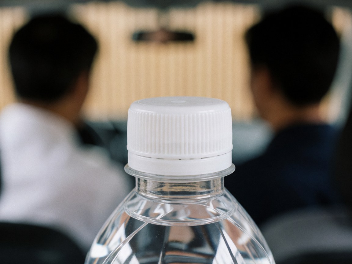 Close-up of a textured water bottle cap with a blurred background featuring light wood walls and two people, suitable for hygiene services.