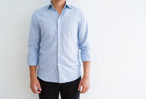 A man wearing a blue and white striped shirt stands against a plain white background, suitable for professional business use.