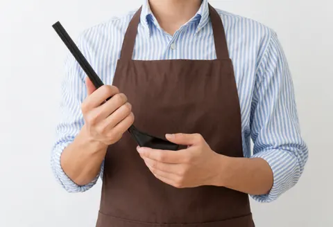 A person wearing a striped shirt and apron holding a kitchen spoon against a white background.