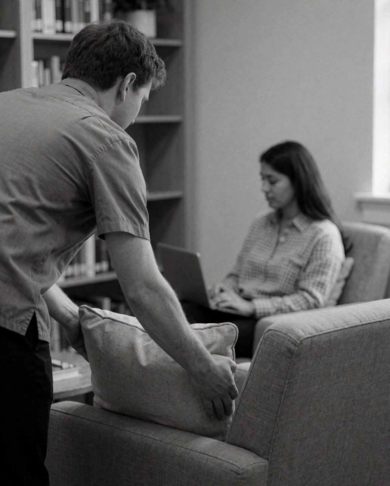 A woman uses a laptop in a calm reading area with bookshelves, gray walls, and comfortable seating.