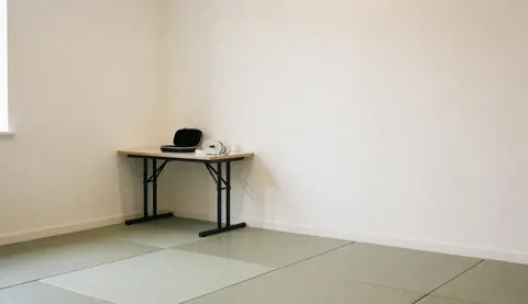 Karate equipment including a mouthguard and gi belt on a wooden table in a dojo with tatami mats and cream walls