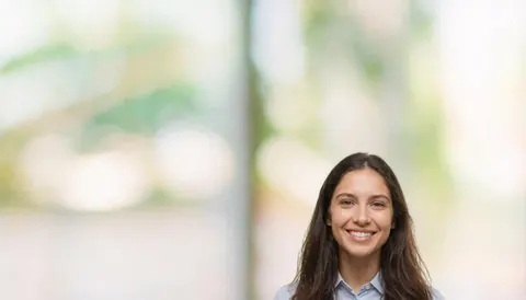 A smiling woman in an office setting with a blurred background featuring greenery, suitable for business text overlays.