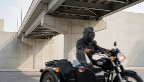 Motorcycle with sidecar positioned beneath a pedestrian bridge featuring steel and concrete structure in an urban setting