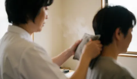 Therapist applying a hot pack to a client's neck in a treatment room with warm white walls and natural light