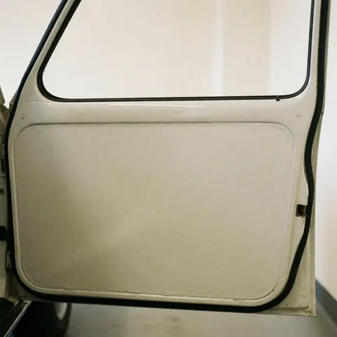 Close-up of a car door featuring smooth, uniform paint with sharp reflections against a warm white wall, ideal for auto body painting services.