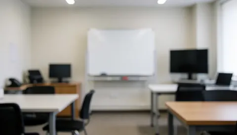Blurred background of a photography workshop featuring tables, chairs, a whiteboard, and monitors, ideal for text overlay.