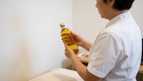 Back view of a professional holding an oil bottle in a white-walled ayurvedic clinic with copy space