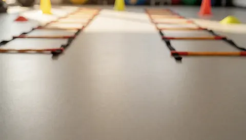 Warmly lit gym floor with an agility ladder and training cones, providing a clean background suitable for text overlays and sports design.