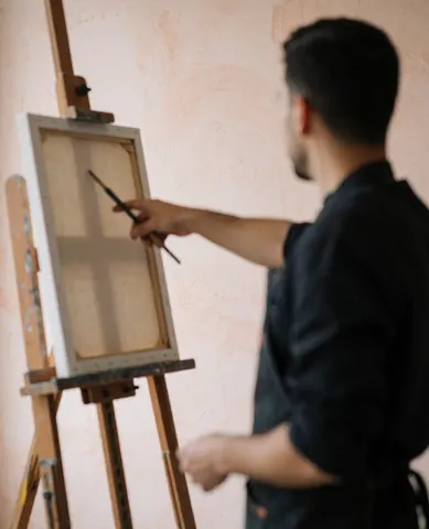 Back view of an artist painting on a wooden easel in a professional studio with light plaster walls