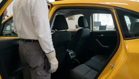 Yellow taxi with open door showing driver from behind and seated passenger in clean modern interior for transport services