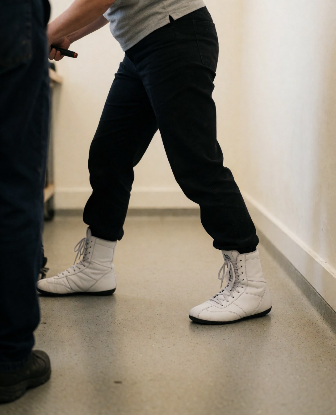 White boxing shoes positioned in a training stance on a rubber floor within a gym setting.