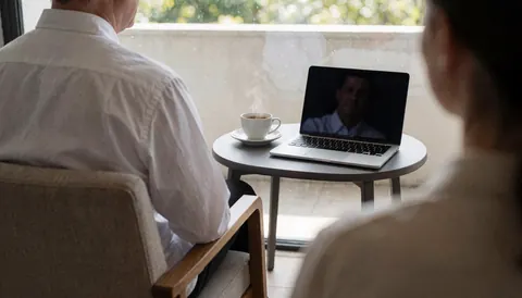 A relaxed customer sits on a balcony with a laptop and coffee cup, enjoying the view from an apartment hotel.