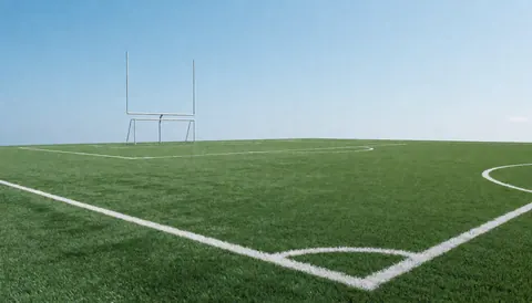 Empty american football field with white lines and goal posts under a clear blue sky, ideal for training.