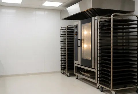 Industrial convection oven in a bakery with tray racks and white tiled walls ready for baking