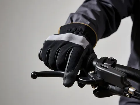 Close-up of a hand wearing a black and gray glove gripping a bicycle handlebar against a gray wall background