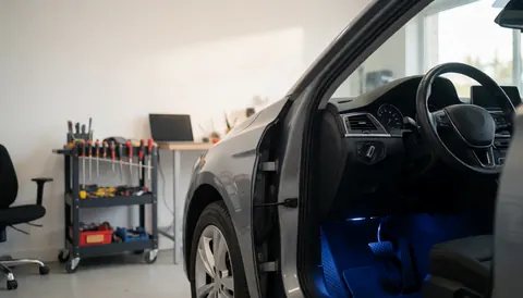 Car interior illuminated with blue lights in a workshop, featuring tools on a cart and an office chair in the background.