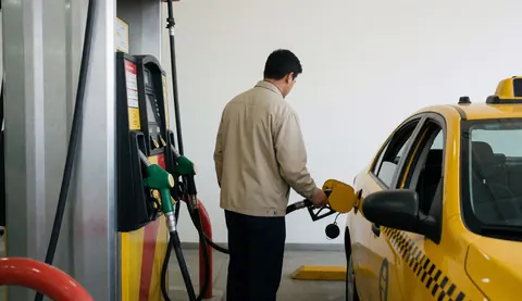 Taxi driver refueling a yellow taxi at a gas station with a white wall background, face not visible