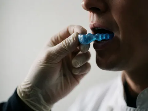 Close-up of a boxing instructor putting a blue mouthguard in his mouth against a white background