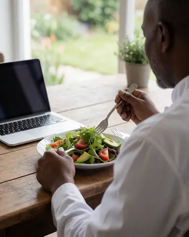 A customer enjoys a fresh salad with tomato and avocado on a rustic wooden table near a garden window with a laptop nearby.
