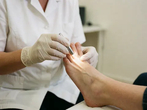 A podiatrist in gloves examines a patient's foot using a medical light in a clean clinic.
