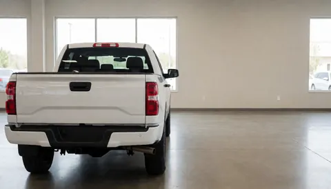 White pickup truck displayed in a car dealership showroom with polished concrete floor and beige walls.