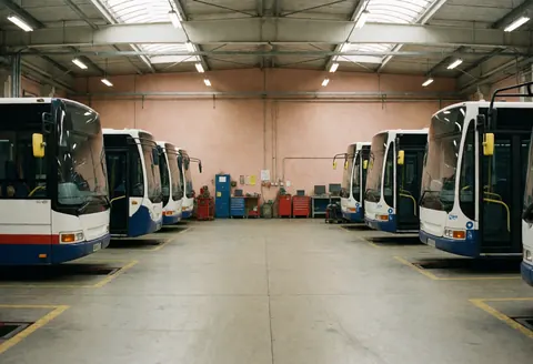 Public transport buses lined up in a depot featuring terracotta walls and visible maintenance tools in the background.