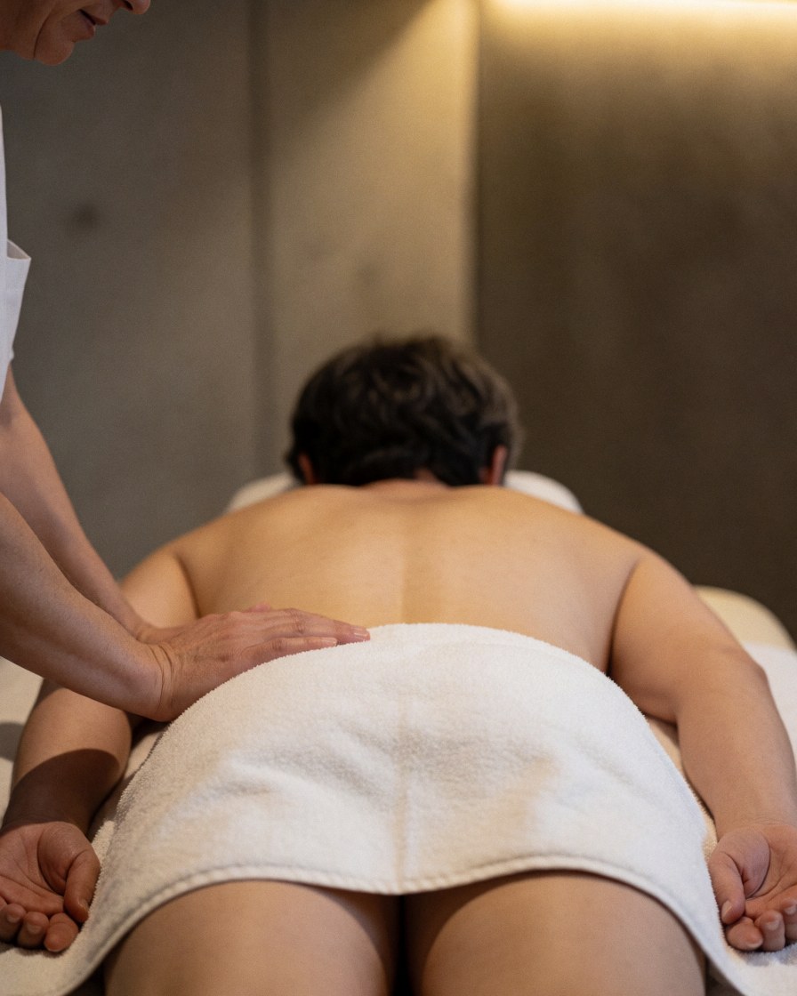 Therapist hands on client back during deep tissue massage in room with concrete walls and warm lighting